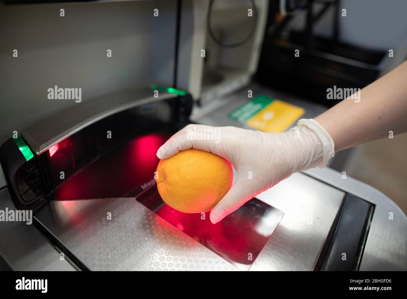 Eine Hand in Einweg-Latex-Handschuh Scannen eine Orange in einem Supermarkt Self-Checkout-Station. Menschen, die Handschuhe tragen, um sich vor Kovid zu schützen Stockfoto
