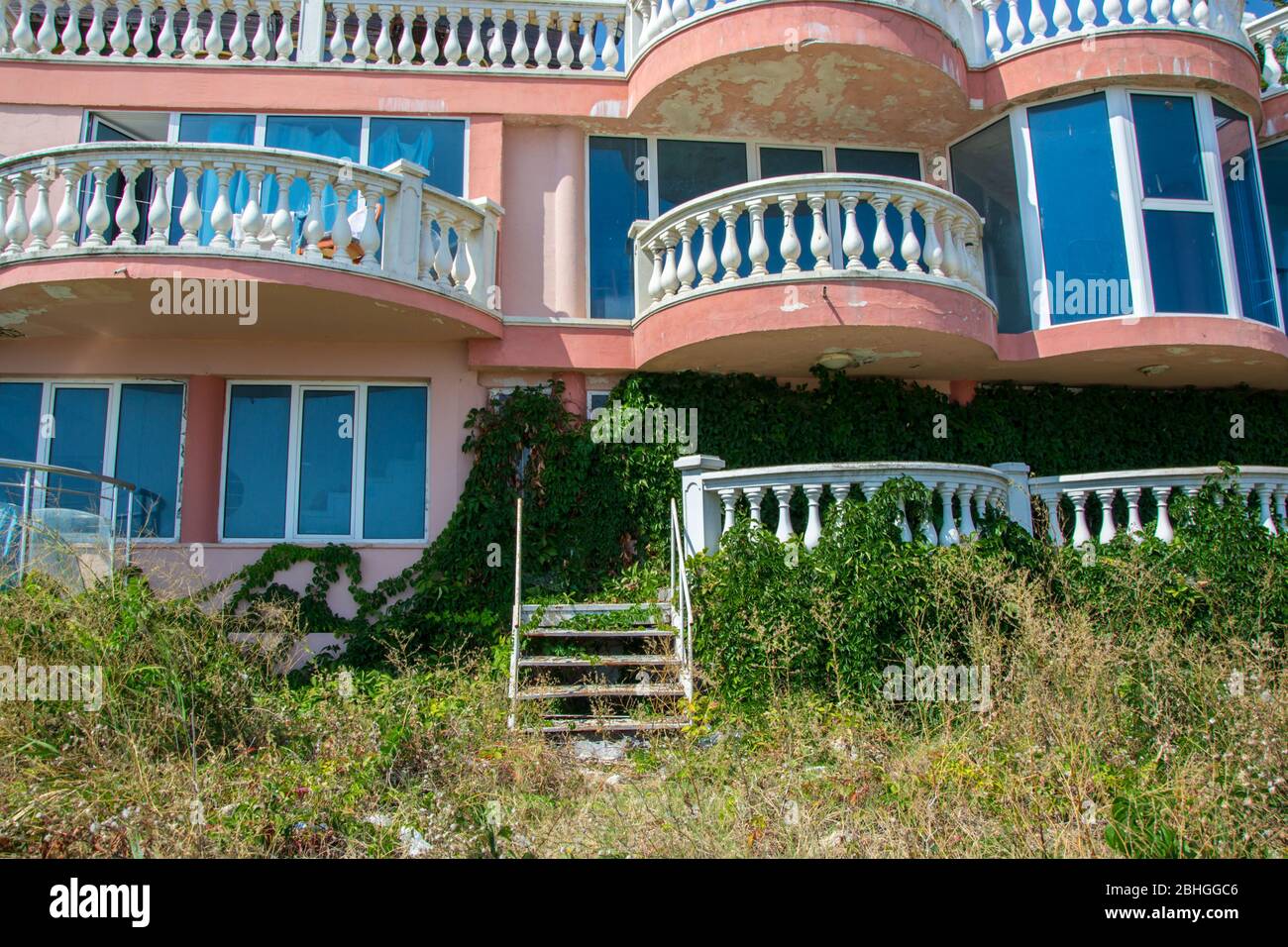 Verlassene Hotel am Strand, mit grünem Gras und kletternden Efeu Pflanze bedeckt, die Natur übernehmen Konzept, Gebäude Fassade Stockfoto