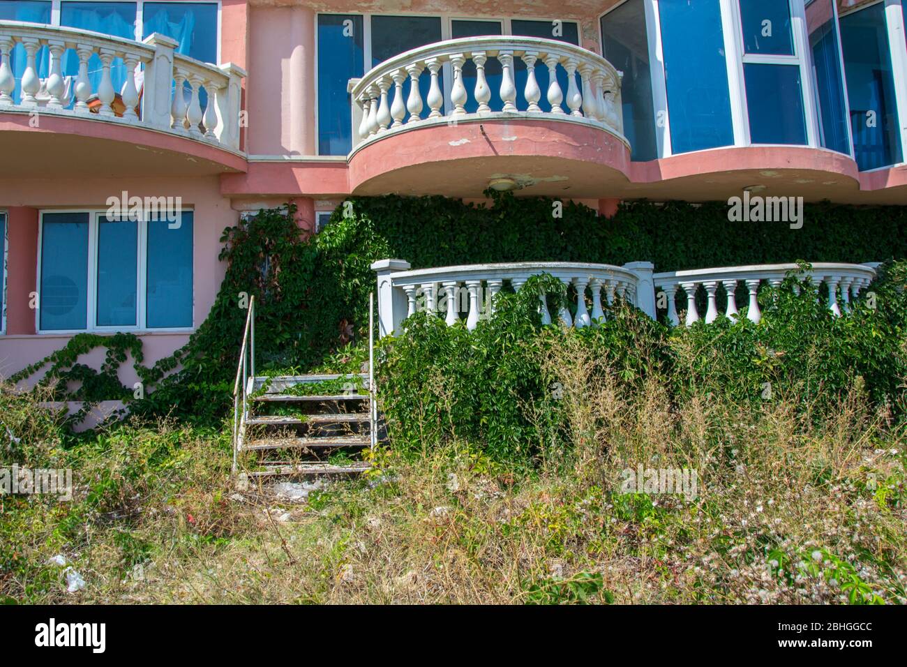 Verlassene Hotel am Strand, mit grünem Gras und kletternden Efeu Pflanze bedeckt, die Natur übernehmen Konzept, Gebäude Fassade Stockfoto