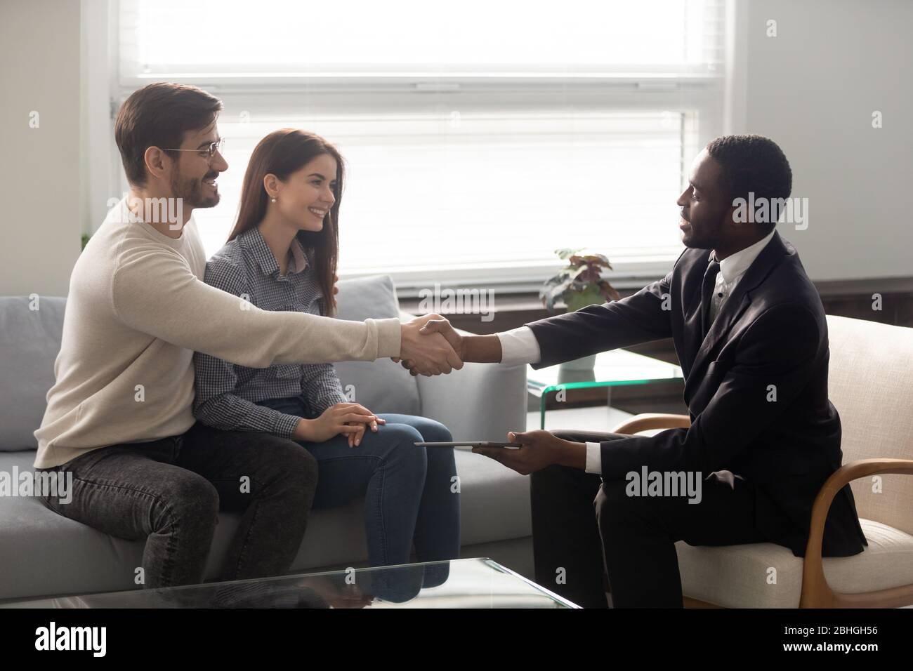 Lächelnder afroamerikanischer Geschäftsmann im Anzug, der mit dem Mann die Hände schüttelt. Stockfoto
