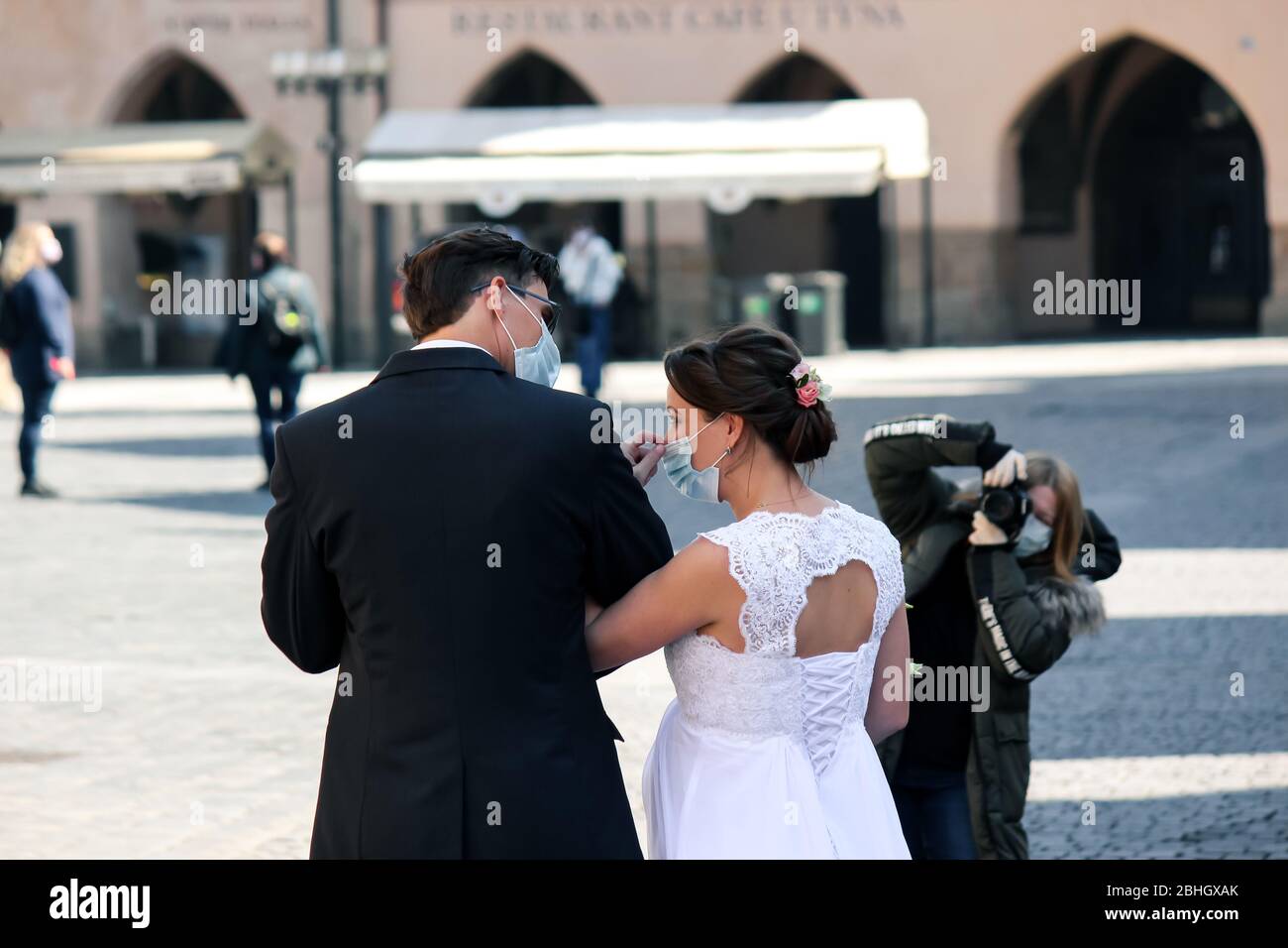 Prag, Tschechische Republik - 23. April 2020: Hochzeitspaar in medizinischen Gesichtsmasken, fotografiert von einem Fotografen mit Gesichtsmaske in der Altstadt. Hochzeit während der Coronavirus-Pandemie. COVID-19 Hochzeiten. Stockfoto