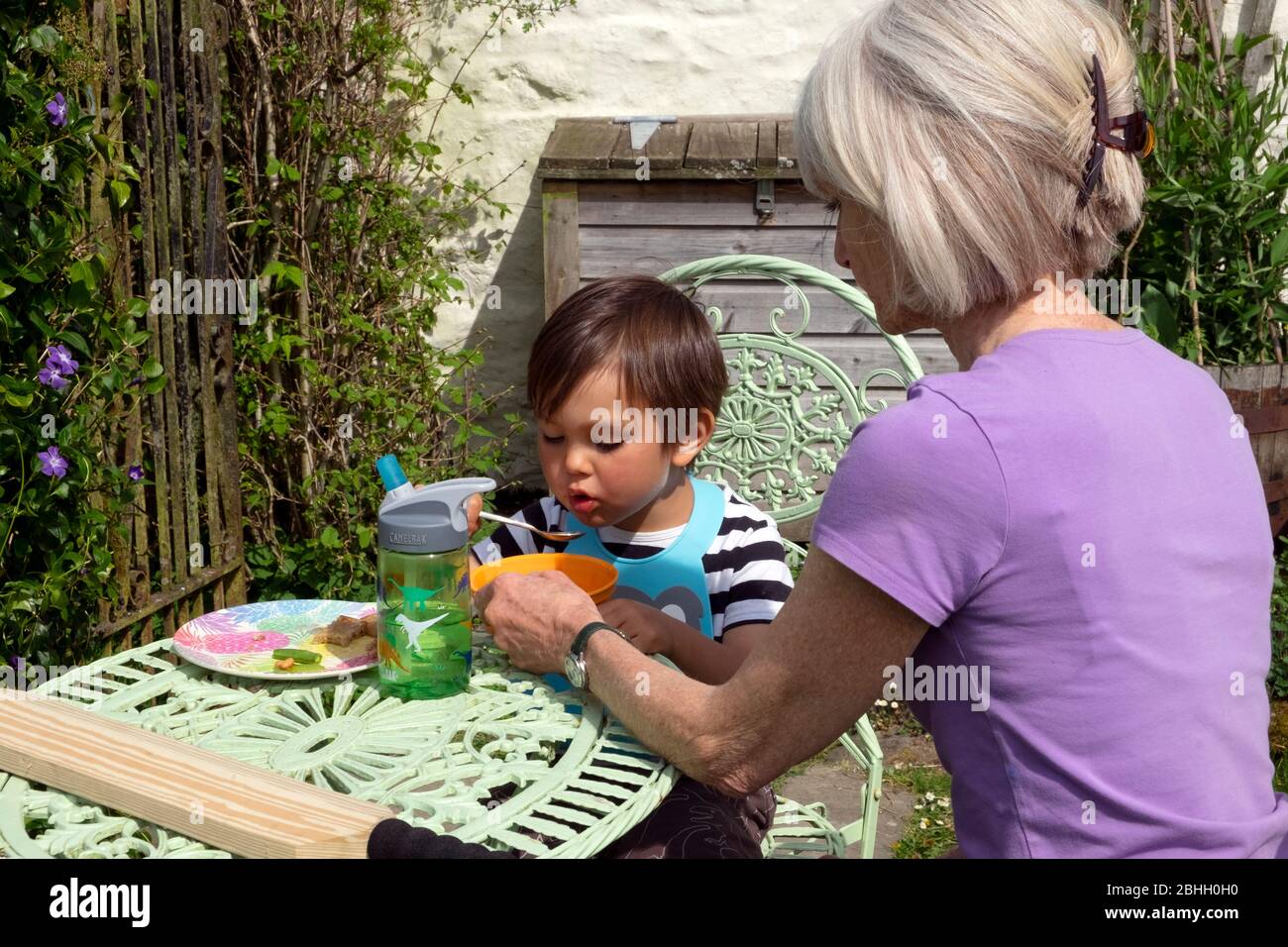 Großmutter sitzt am Tisch im Garten helfen Kind Junge 3 Jahre, um sein Mittagessen Essen während Covid 19 Lockdown in Carmarthenshire Wales UK KATHY DEWITT Stockfoto