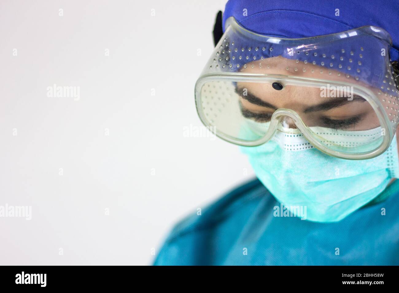 Desolate Krankenschwester, Blick nach unten, mit Schutzausrüstung für Coronavirus, Maske, Brille und OP-Kappe. Stockfoto