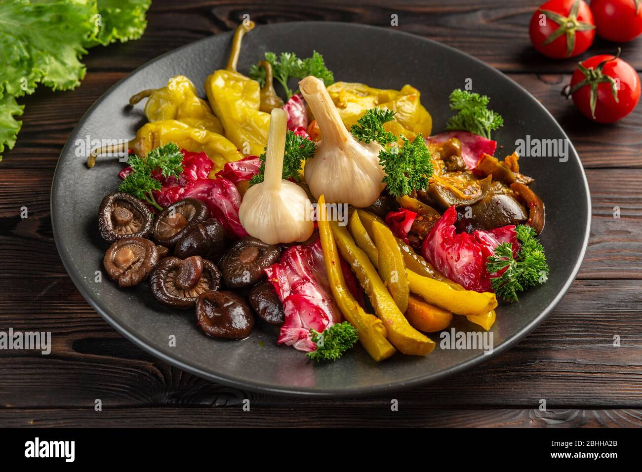 Gesalzenes und eingelegtes Gemüse: Auf einem schwarzen Teller auf Holzhintergrund Stockfoto