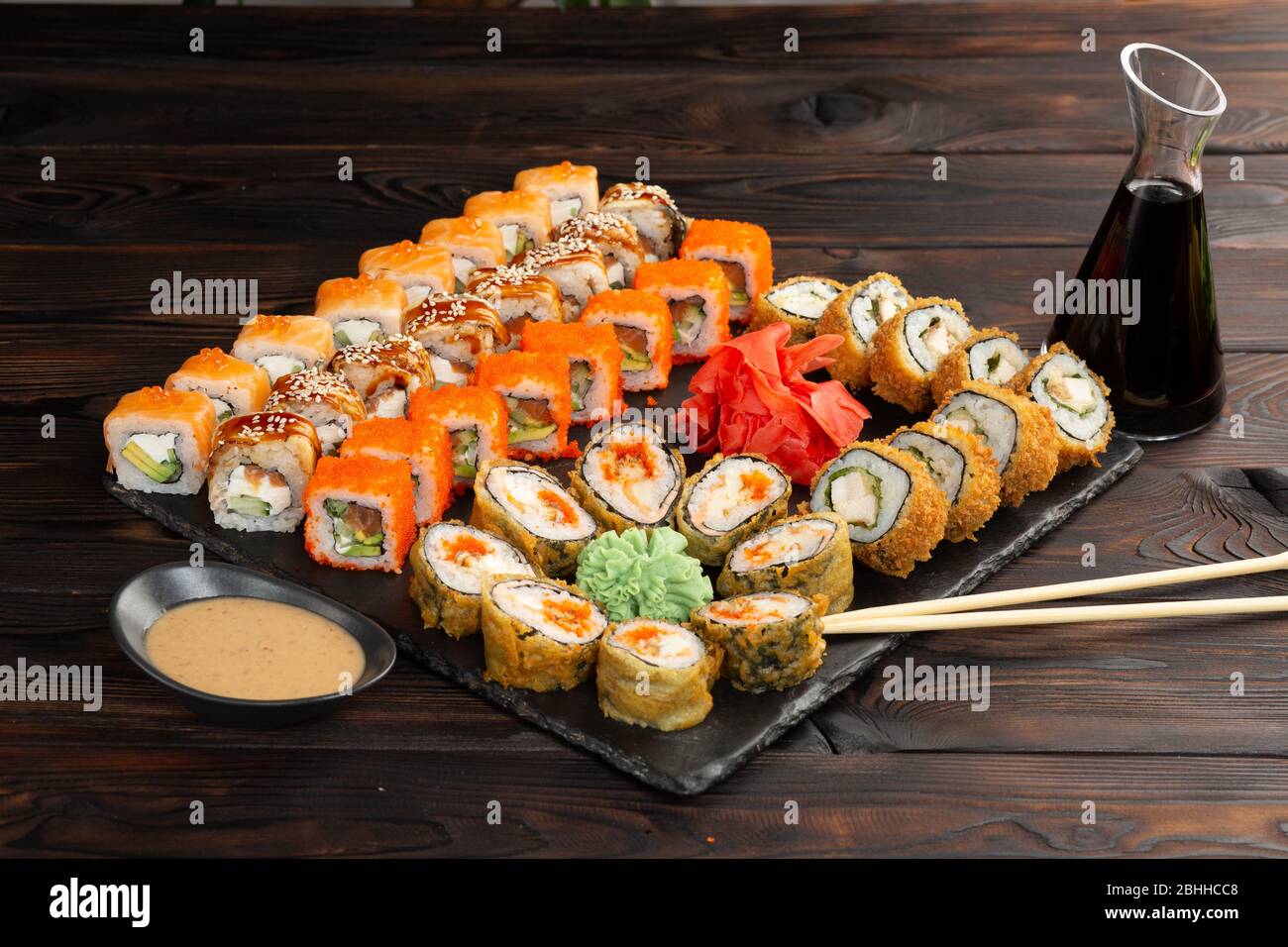 Sushi-Set mit Sauce und Essstäbchen auf einem schwarzen Brett auf dunklem Holzhintergrund Stockfoto
