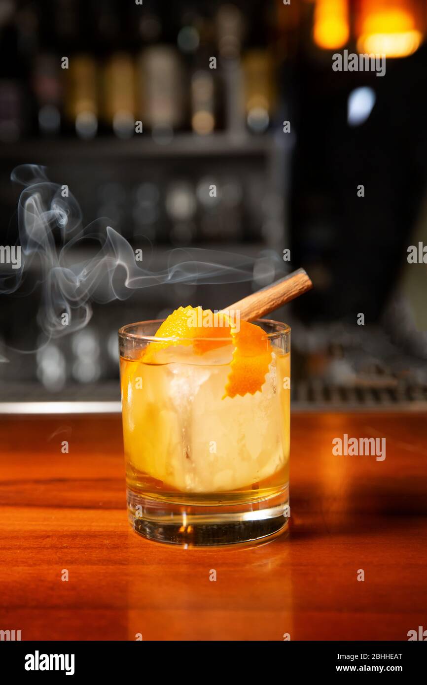 Orangencocktail mit Eiswürfel und Orangenschale. Im Glas ist ein Zimtstab, aus dem Rauch entsteht. Stockfoto