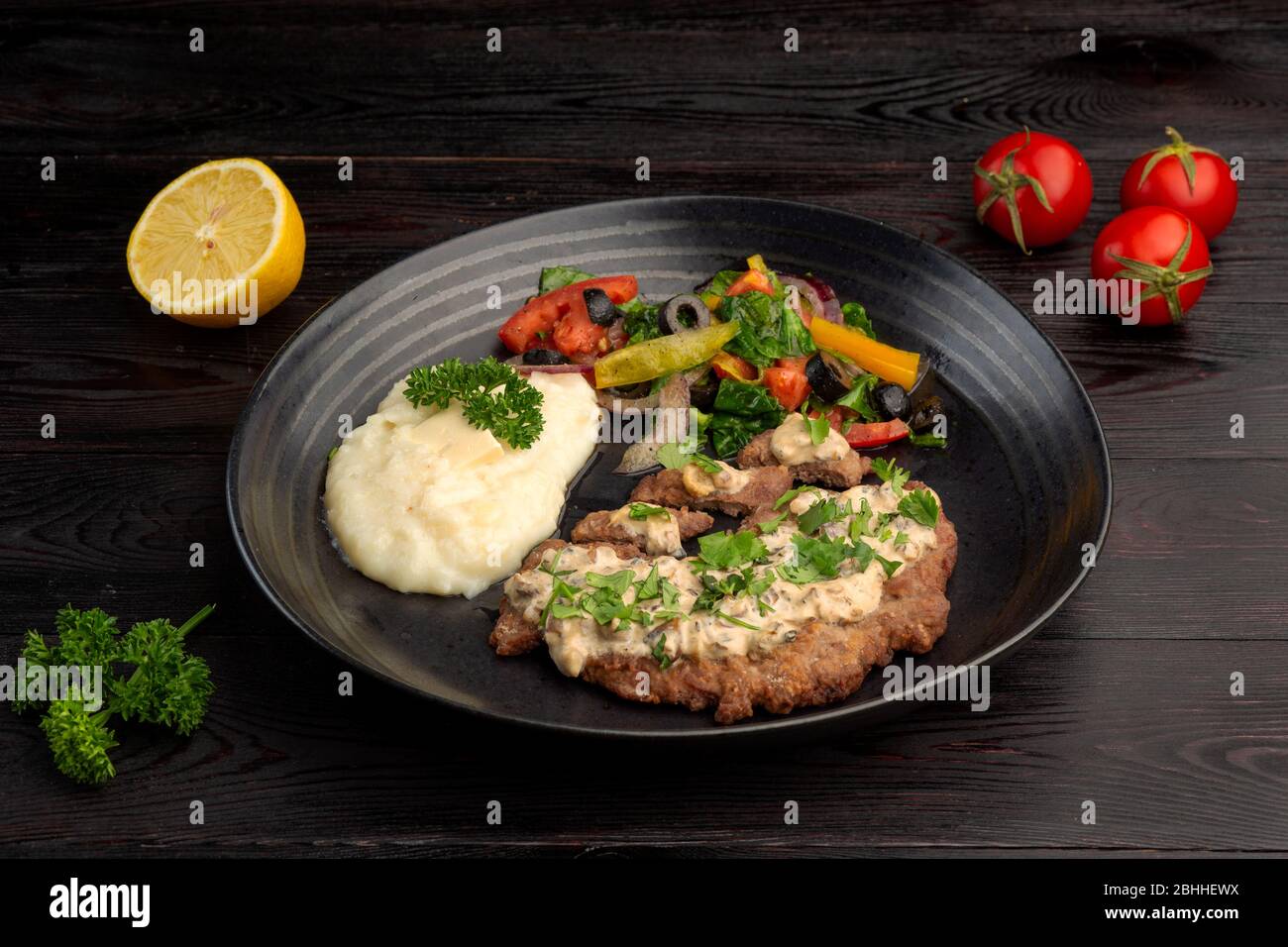 Gebratenes Steak und Kartoffelpüree mit frischem Gemüsesalat auf einem runden Teller auf dunklem Holzhintergrund Stockfoto