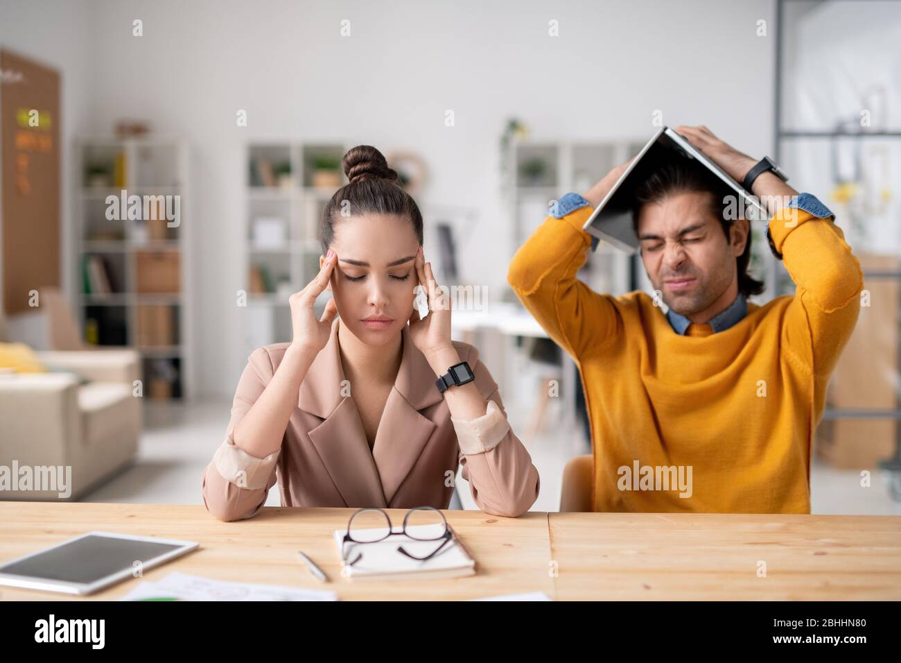 Verwirrt junge Kollegen müde von der Arbeit sitzen am Tisch und Kopfschmerzen fühlen, Problem mit dem Projekt wegen Coronavirus Stockfoto