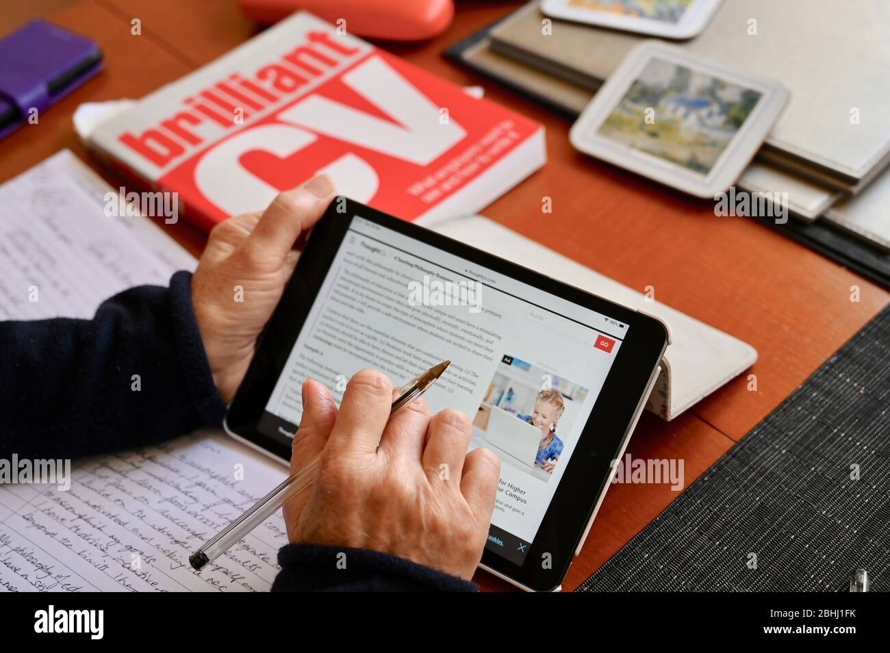 Eine ältere Frau bezieht sich auf das Internet, während sie eine Bewerbung vorbereitet. Stockfoto