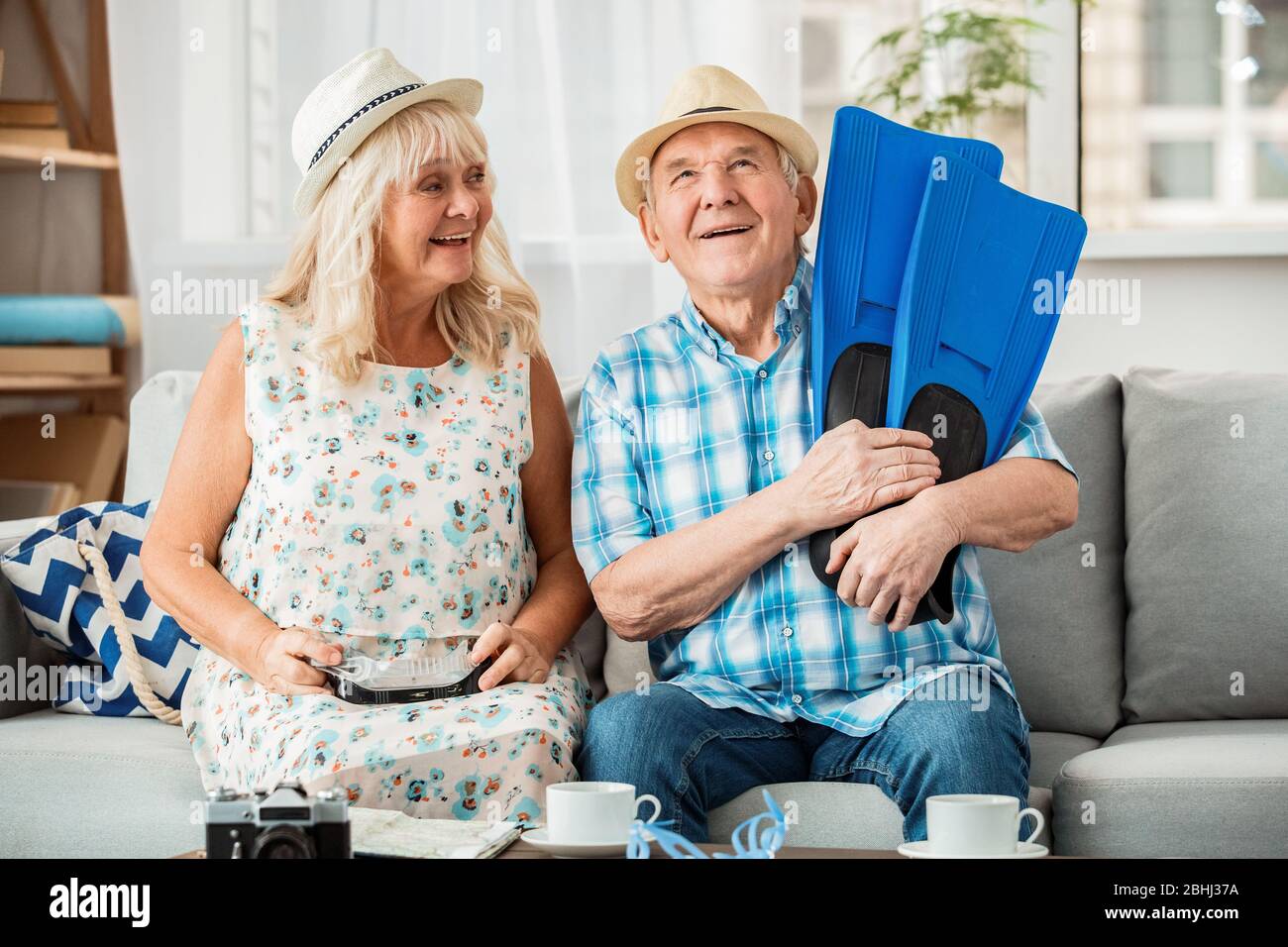 Ältere Paar sitzt in Reisebüro sitzen Hüte Frau mit Schwimmbrille während Mann hält Flossen träumerisch Stockfoto