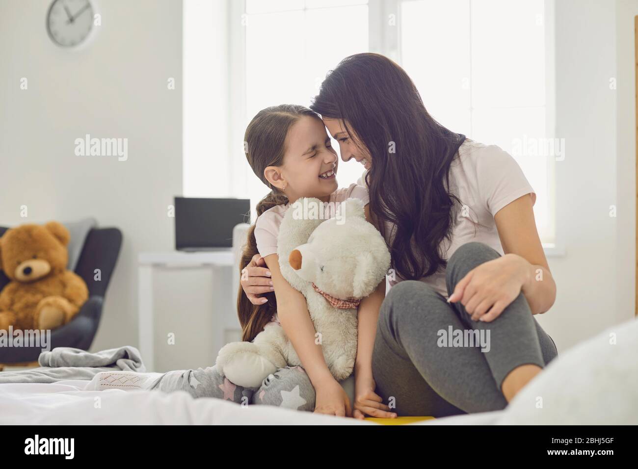 Alles Liebe zum Muttertag. Frohe Familie. Mutter und Tochter umarmen sich, während sie auf dem Bett in einem weißen Zimmer sitzen. Stockfoto