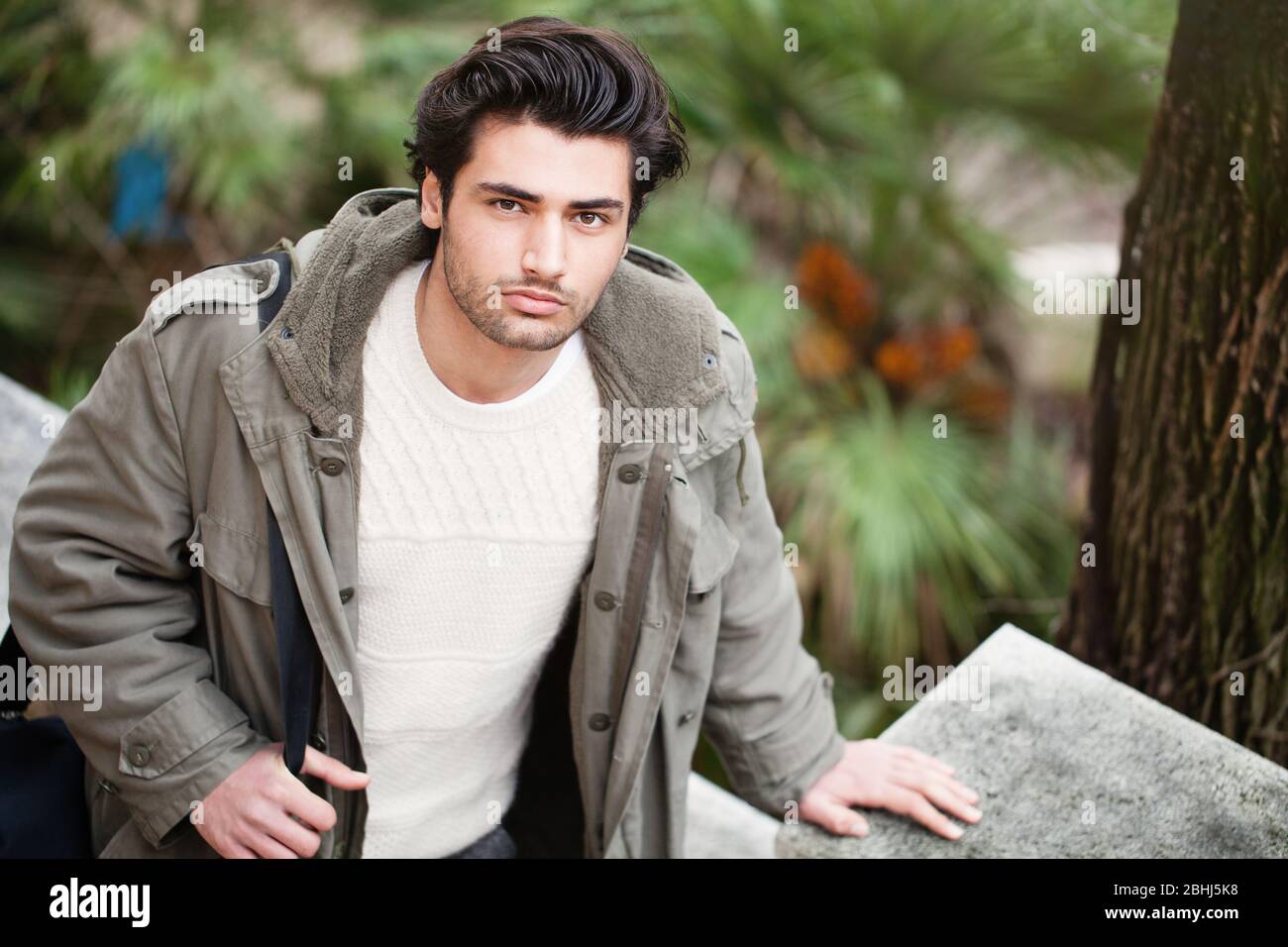 Schöner junger italienischer Mann, der auf der Straße läuft. Von oben gesehen. Stylische Haare und Mantel im Freien mit Winterjacken, Umhängetasche und Herbstklumpen Stockfoto