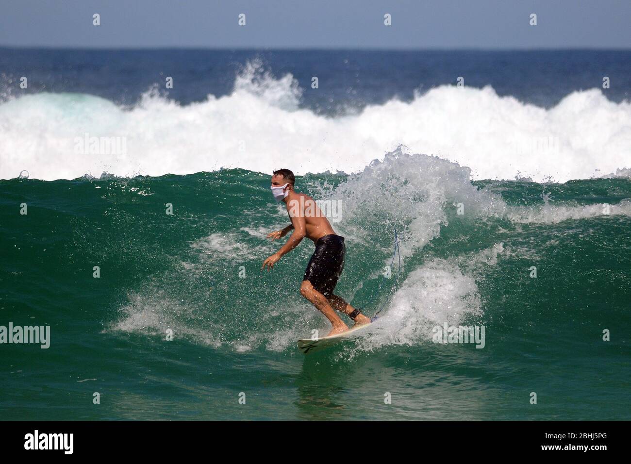 Rio de Janeiro, Brasilien, 25. April 2020. Surfer reiten Welle mit Coronavirus-Schutzmaske, am Strand Barra da Tijuca, im Westen der Stadt ​​the Stockfoto