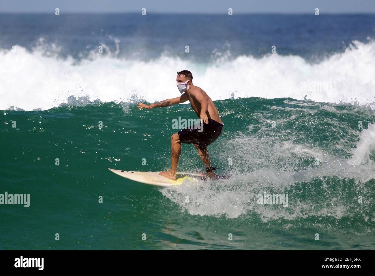 Rio de Janeiro, Brasilien, 25. April 2020. Surfer reiten Welle mit Coronavirus-Schutzmaske, am Strand Barra da Tijuca, im Westen der Stadt ​​the Stockfoto