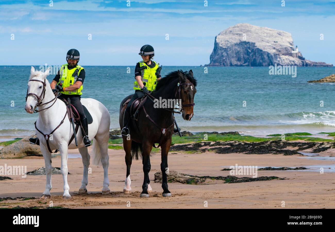 North Berwick, Schottland, Großbritannien. 26. April 2020. Berittene Polizisten patrouillieren heute Nachmittag an den Stränden von North Berwick in East Lothian. Die Pferde Inverness (dunkel) und Edinburgh reisten von ihren Ställen in Stewarton in Ayrshire für den heutigen Spaziergang. Die Strände waren jedoch sehr ruhig und die Pferde mussten sich mit den wenigen Leuten draußen fotografieren lassen. Abgebildet; montierte Polizei am Strand mit Bass Rock in der Ferne. Iain Masterton/Alamy Live News Stockfoto