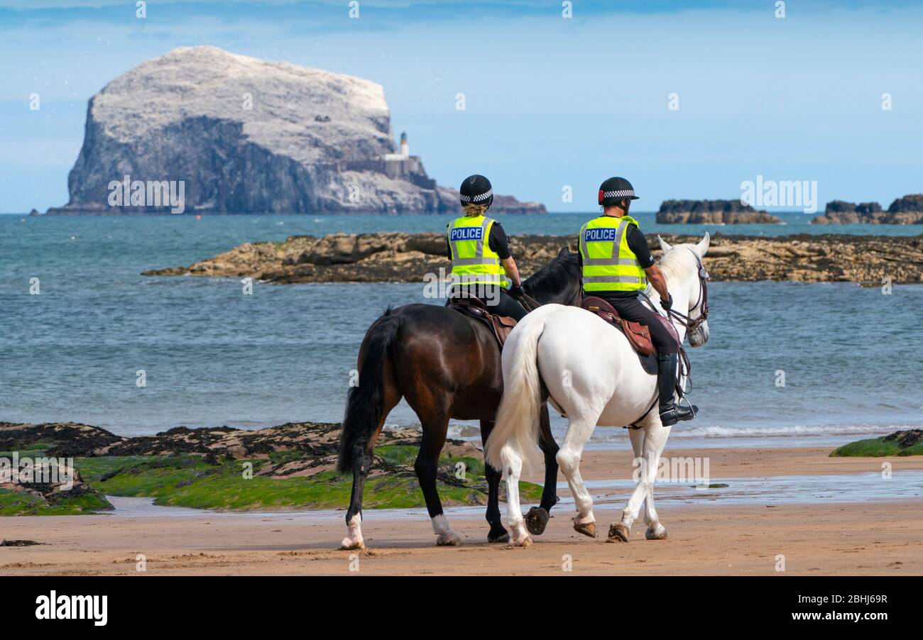 North Berwick, Schottland, Großbritannien. 26. April 2020. Berittene Polizisten patrouillieren heute Nachmittag an den Stränden von North Berwick in East Lothian. Die Pferde Inverness (dunkel) und Edinburgh reisten von ihren Ställen in Stewarton in Ayrshire für den heutigen Spaziergang. Die Strände waren jedoch sehr ruhig und die Pferde mussten sich mit den wenigen Leuten draußen fotografieren lassen. Abgebildet; montierte Polizei am Strand mit Bass Rock in der Ferne. Iain Masterton/Alamy Live News Stockfoto