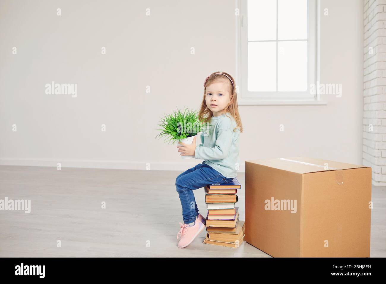 Ein Mädchen mit einer Blume sitzt auf den Kisten für den Umzug in ein neues Haus. Stockfoto