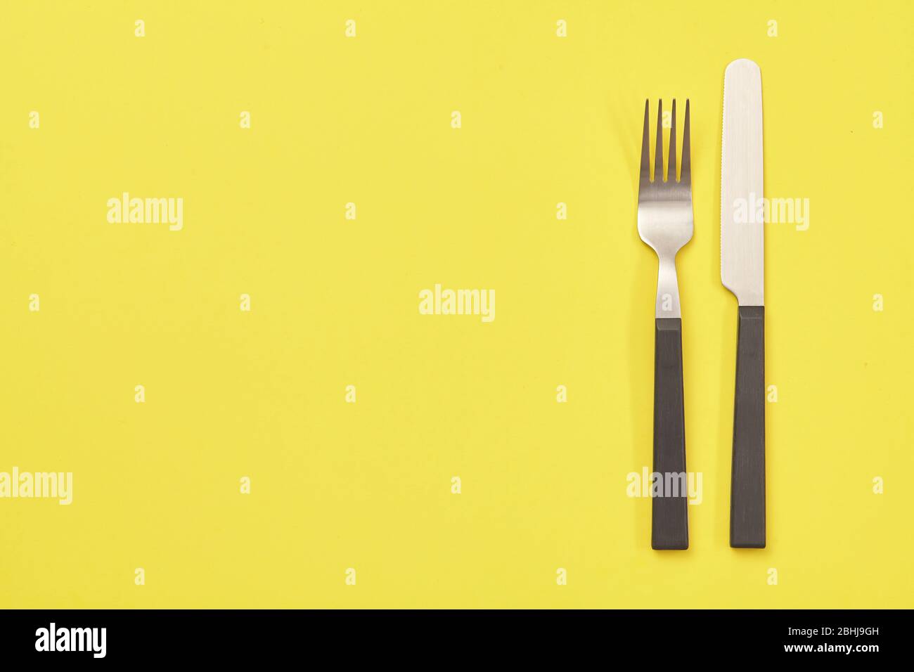 Schwarzes Messer und Gabel auf gelbem Hintergrund. Draufsicht Stockfoto