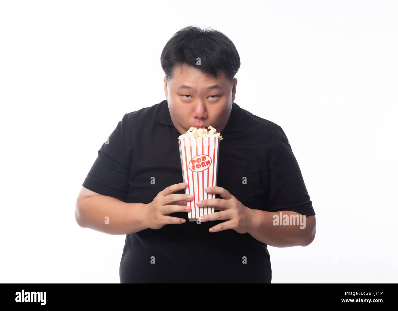 Lustige junge asiatische Fett Mann in schwarzen Poloshirt essen Popcorn isoliert auf weißem Hintergrund. Stockfoto