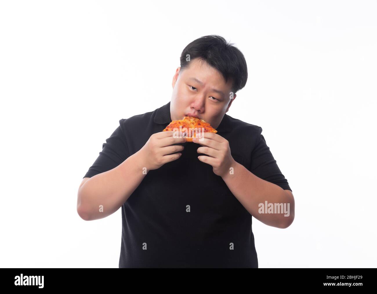 Glücklich junge asiatische Fett Mann in schwarz Polo-Shirt essen Pizza isoliert über weißem Hintergrund. Stockfoto