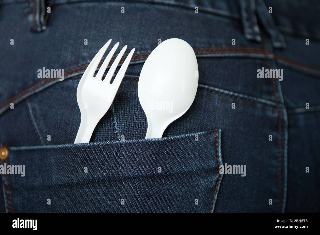 Take Out Food Concept mit blauer Denim Jeans mit weißer Gabel und Löffel in der Tasche. Wiederverwendbarer Kunststofflöffel und Gabel an der Tasche. Sichere Umgebung Stockfoto