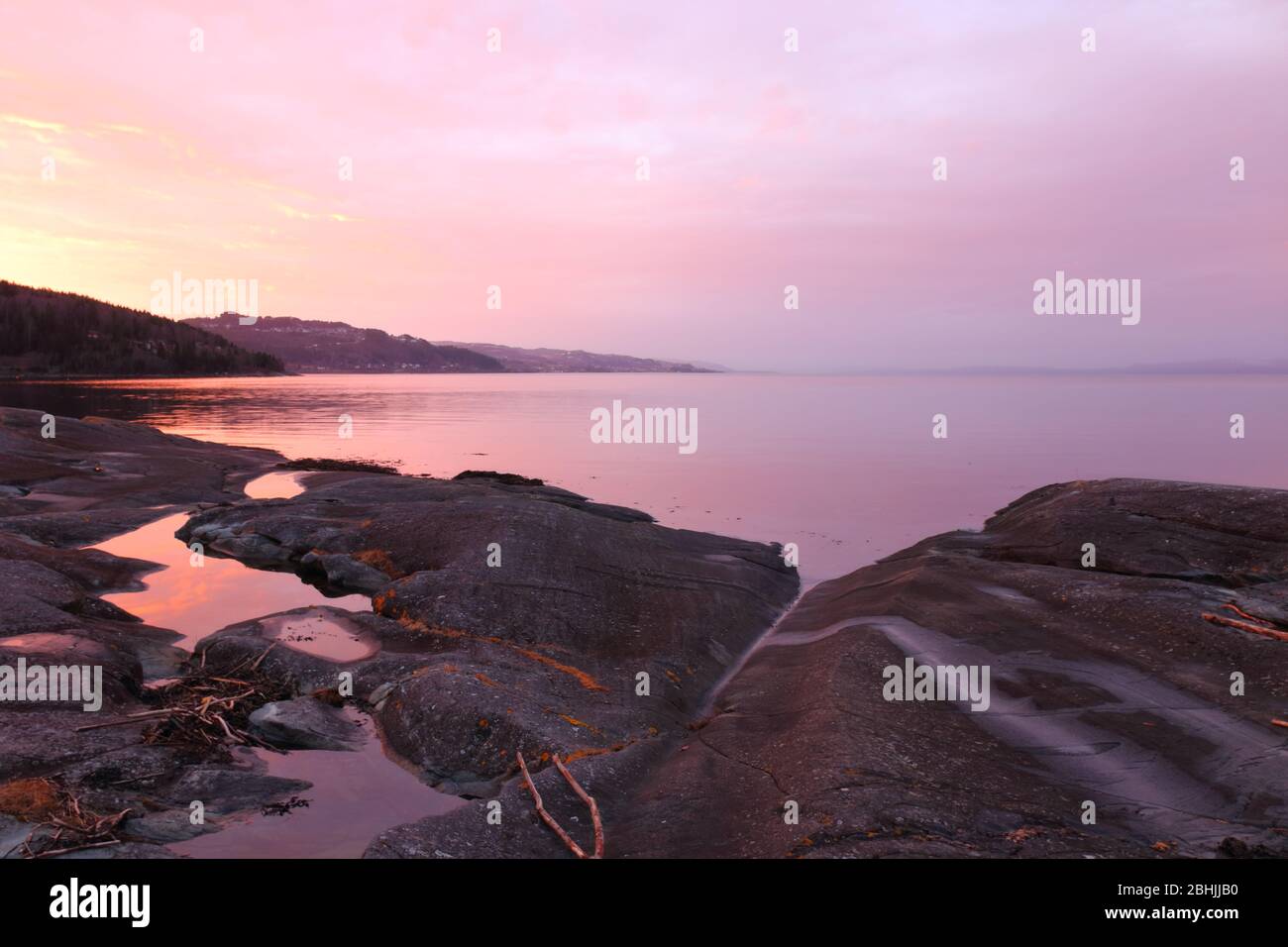 Winteruntergang mit stimmungsvollen Farben und Reflexionen an den felsigen Ufern des Trondheimsfjords, Flatholmen, Norwegen. Stockfoto