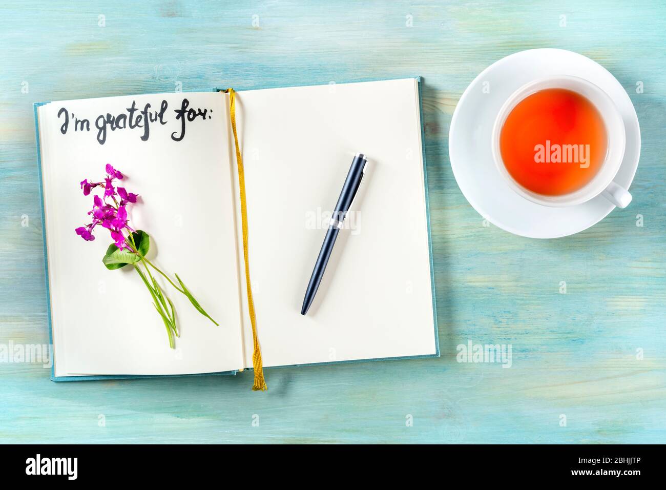 Dankesjournal mit Stift und einer Tasse Tee, mit dem handgeschriebenen Satz, für den ich dankbar bin, und einer Blume, von oben geschossen Stockfoto