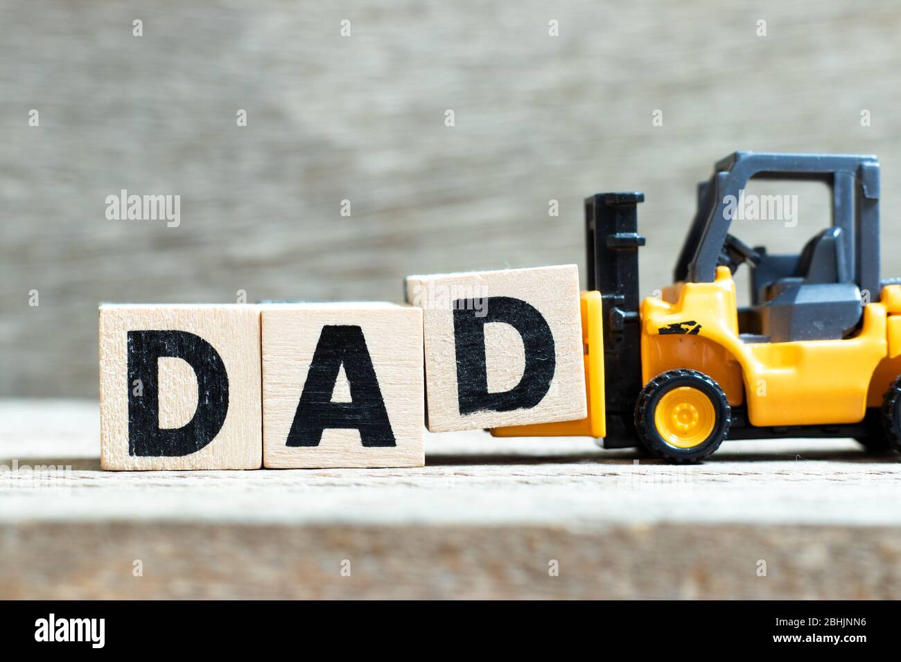 Der Gabelstapler von Toy hält den Buchstabenblock d, um das Wort "Papa" auf dem Holzhintergrund fertigzustellen Stockfoto