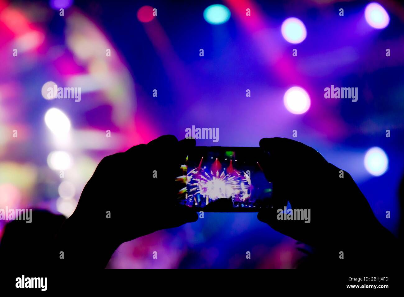 Das Sammeln von digitalem Speicher verliert die Fähigkeit, anwesend zu sein, Silhouette einer Person, die die Lichteffekte der Konzertbühne mit dem Smartphone aufnimmt Stockfoto