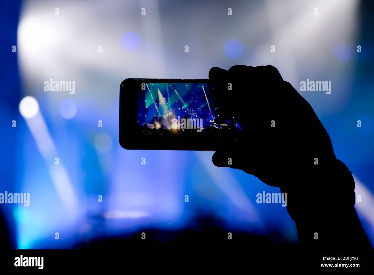 Das Sammeln von digitalem Speicher verliert die Fähigkeit, anwesend zu sein, die Silhouette einer Person, die die Konzertbühne mit dem Smartphone dreht Stockfoto