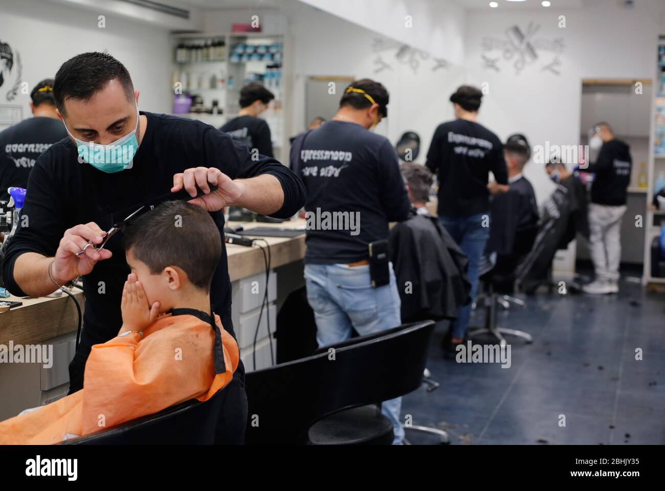 Modin, Israel. April 2020. Israelische Barbiere, die Gesichtsmasken tragen, arbeiten am 26. April 2020 in einem Friseurladen in der zentralisraelischen Stadt Modiin. Alle Straßenläden in Israel, einschließlich Friseur und Schönheitssalons, haben die Genehmigung der Regierung erhalten, ab Samstagabend wieder zu öffnen. (Foto von Gil Cohen Magen/Xinhua) Stockfoto