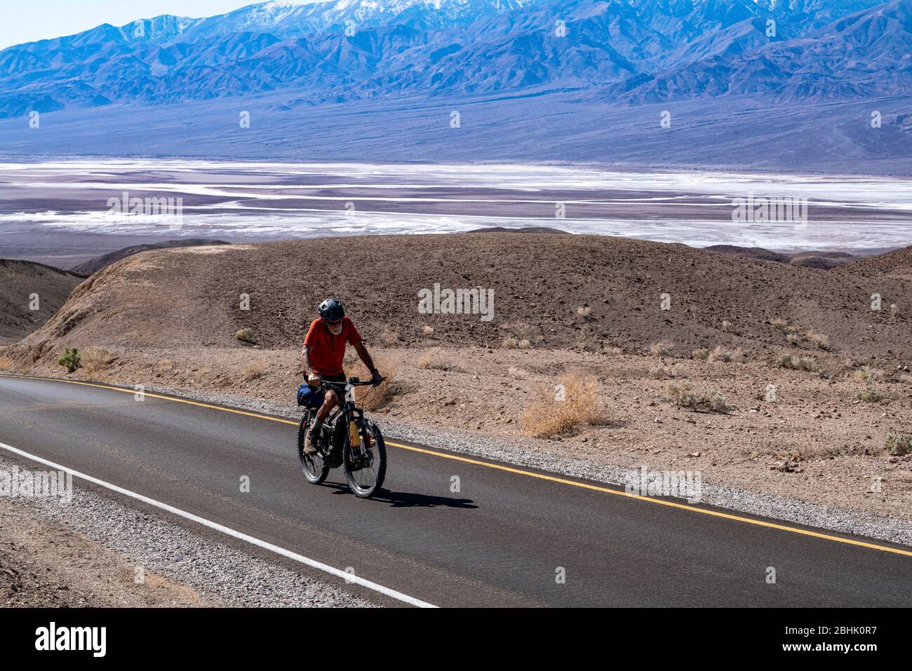 Ein einsam älterer Radfahrer hält sich auf dem Aufstieg entlang des Artist's Palette Drive im Death Valley National Park durch Stockfoto