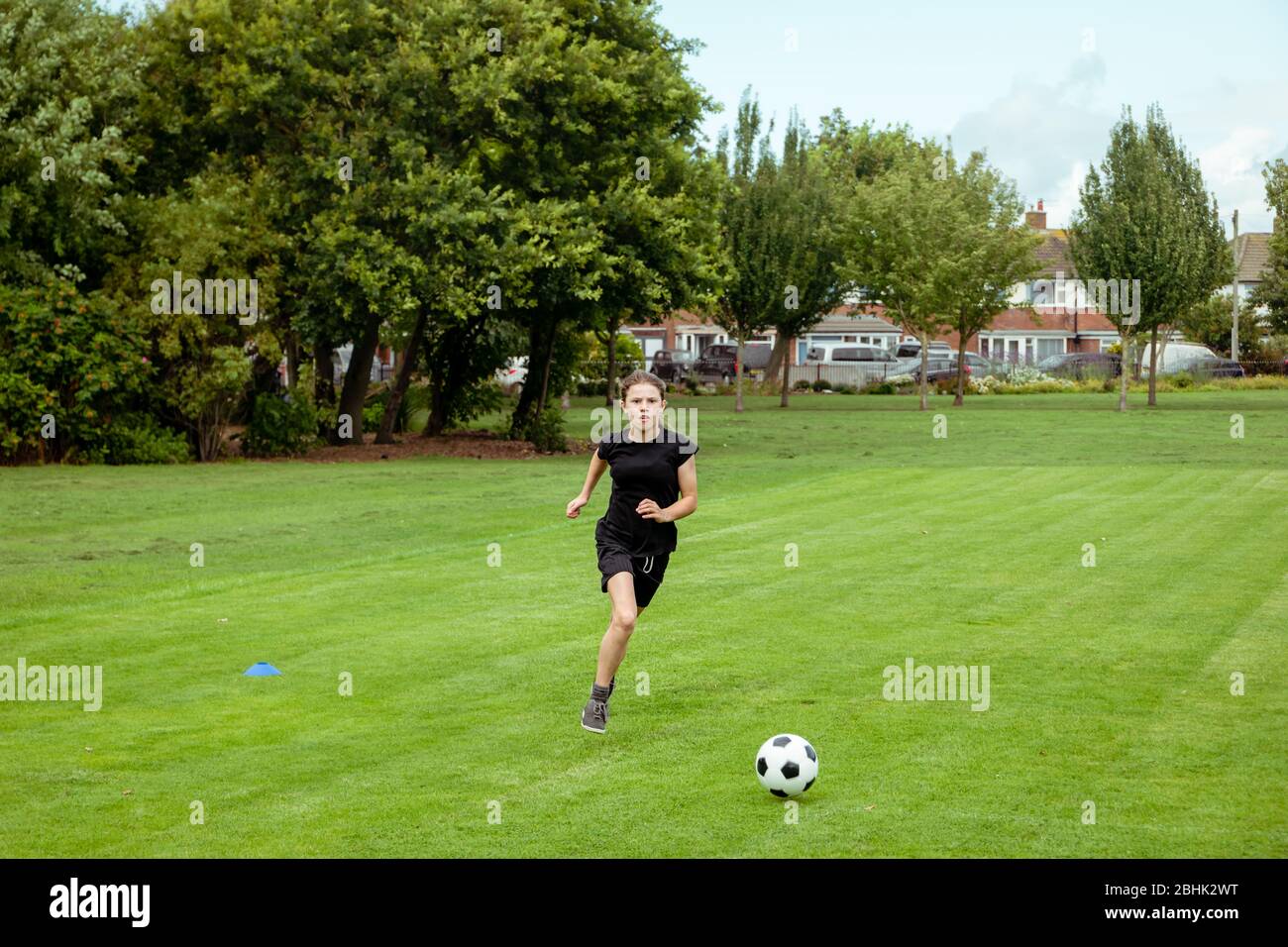 Ein Teenager-Mädchen, das in einem lokalen Park Fußball praktiziert und trainiert Stockfoto