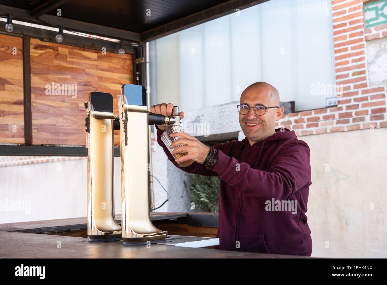 Kaukasischer Erwachsener Mann ohne Haare und trägt Gläser funktioniert lächelnd und glücklich serviert ein Bier in einer Bar. Stockfoto