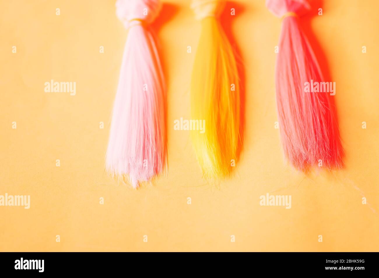 Mehrfarbige, gerade lange Haare, Perücken für handgefertigte Puppen auf gelbem Hintergrund. Handarbeit, Hobby, Freizeitkonzept. Draufsicht. Farbige Haarsträhnen. Stockfoto