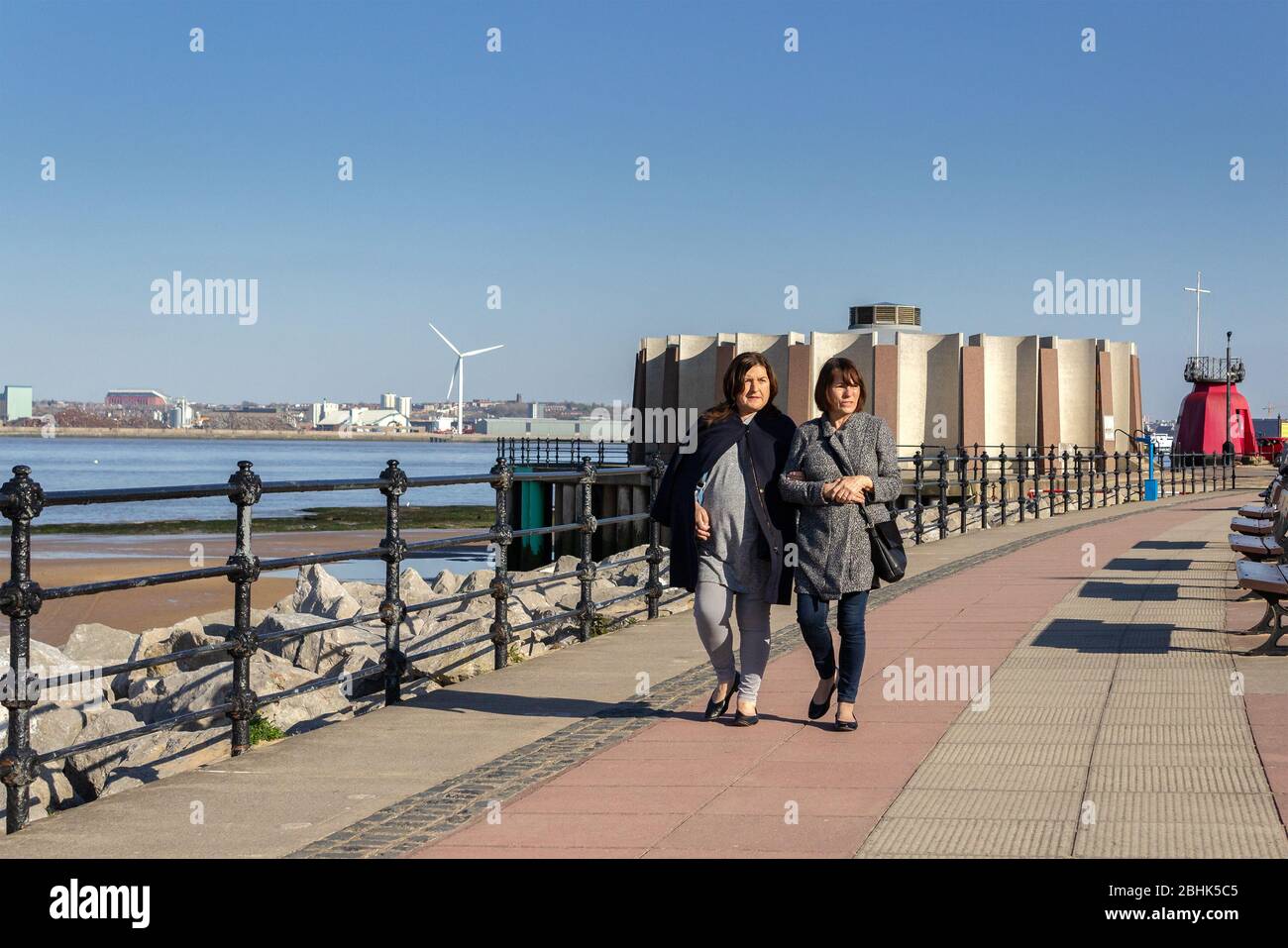 Zwei Frauen, die entlang der Promenade von New Brighton am Fluss Mersey, Wirral Peninsula, spazieren Stockfoto