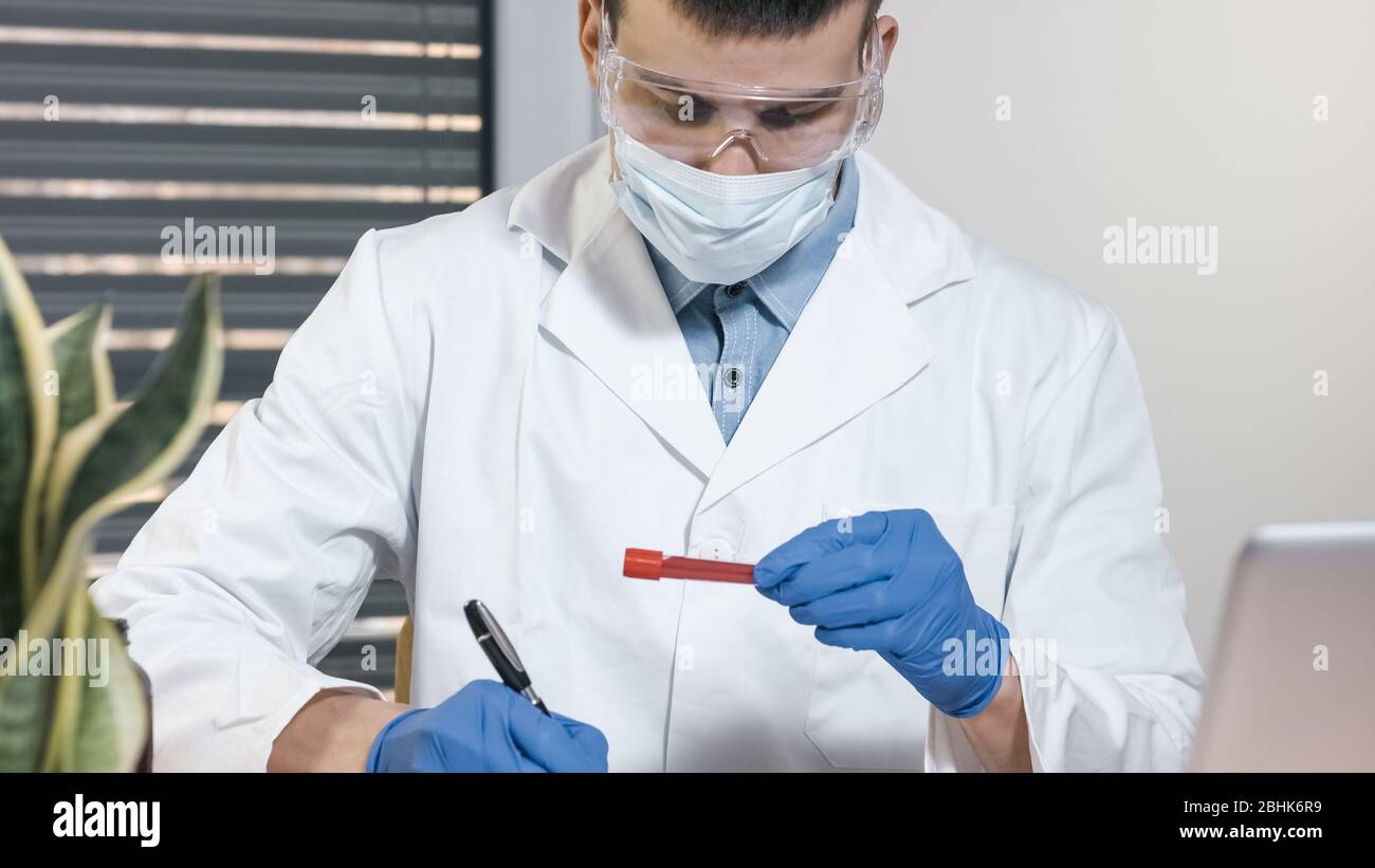 Hand eines Arztes, der eine Blutprobe hält und an Akten schreibt. Stockfoto