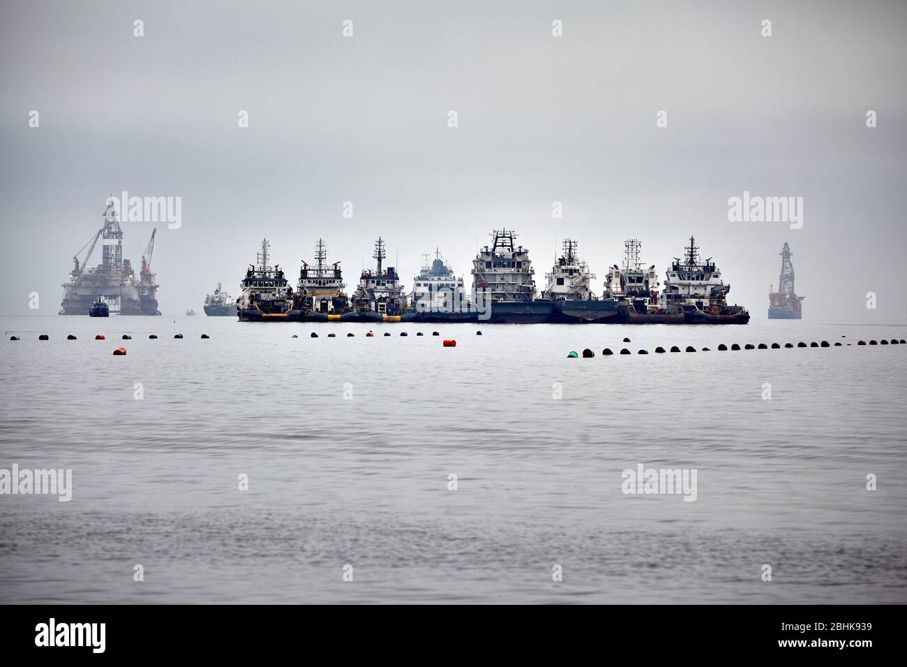 Offshore-Plattformen und Schlepper sind in der Fahrbahn in der Walvisbucht Lagune. Stockfoto