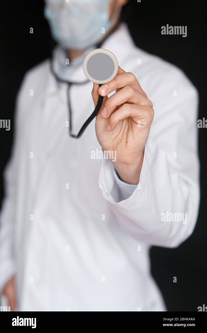 Männlicher Doktor auf schwarzem Hintergrund mit einem Stethoskop in den Händen Nahaufnahme. Stockfoto