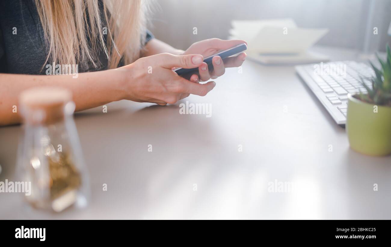 Junge Frau sitzt an einem Schreibtisch und tickt auf einem Smartphone, selektive Fokussierung Stockfoto