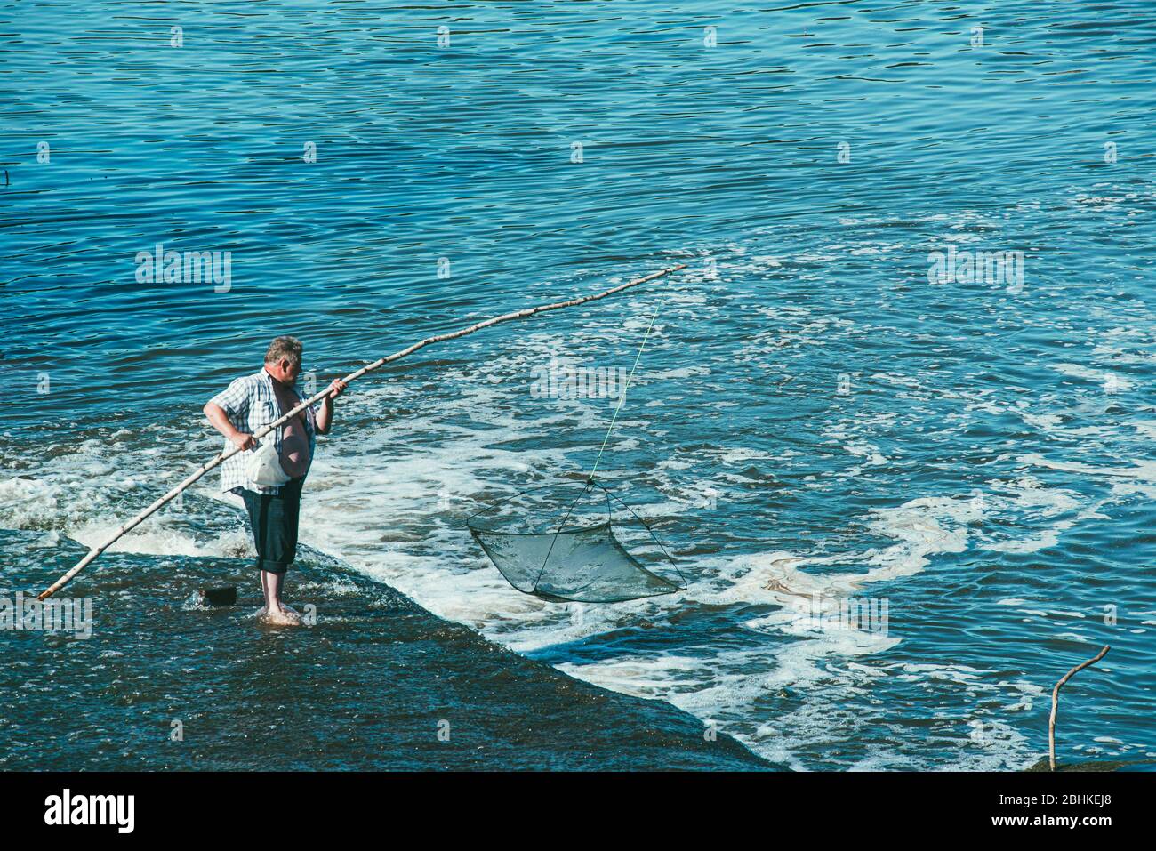 MOSKAU, RUSSLAND 07. JULI 2014: Ein älterer Mann an einem Wasserfall fängt Fische mit einem Netz auf einem Stock Stockfoto