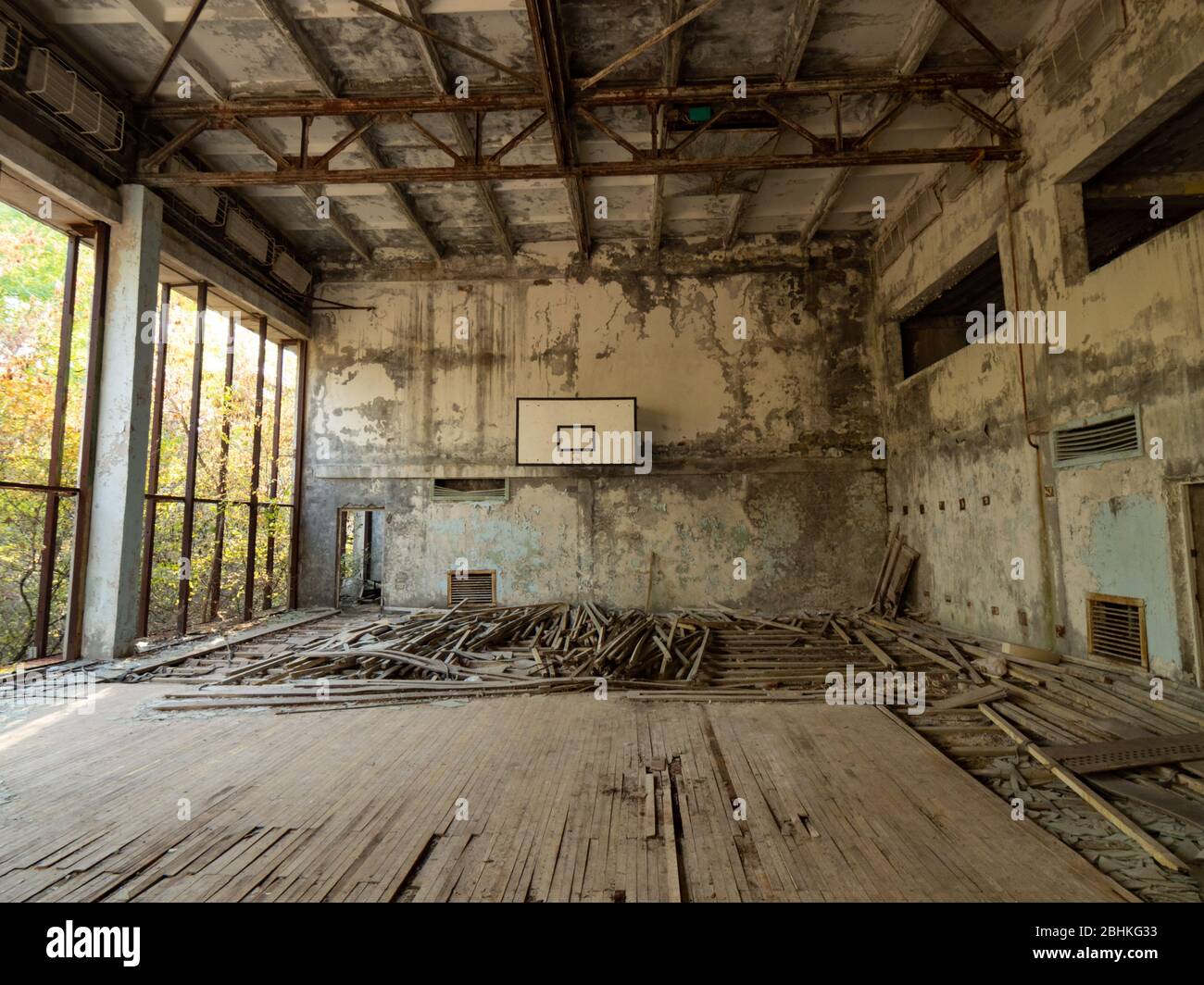 Verlassene leere Turnhalle in der Schule in Pripjat bei Tschernobyl, Ukraine. Die Umgebung des Fitnessstudios ist mit Bäumen und Büschen überwuchert. Stockfoto