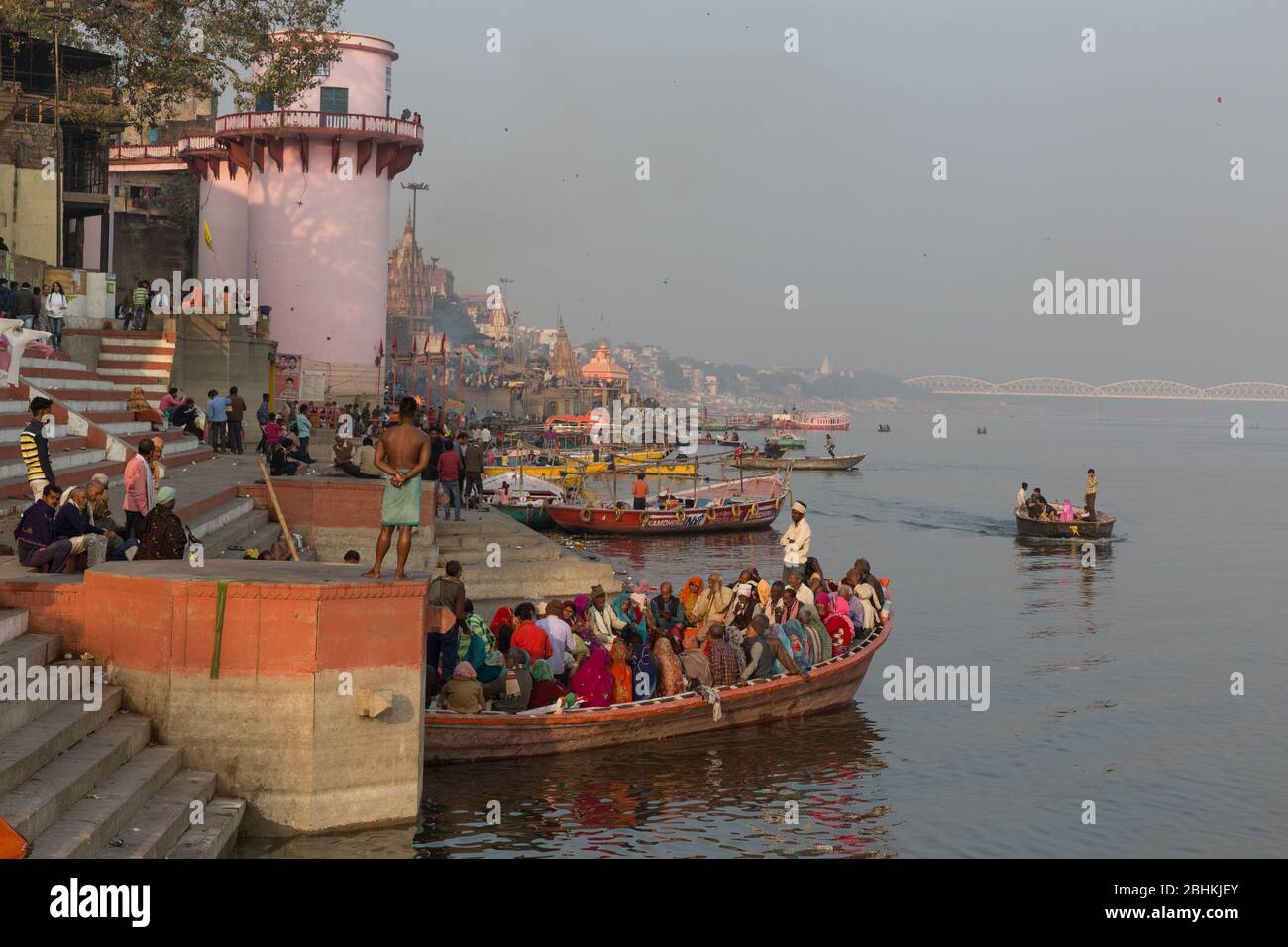Ein Blick auf den Fluss Ganges bei Dämmerung im Sommer in der Nähe von Varanasi, Indien. Leute, die abends in Booten fahren, um die Aussicht auf Ghats am Flussufer zu sehen Stockfoto