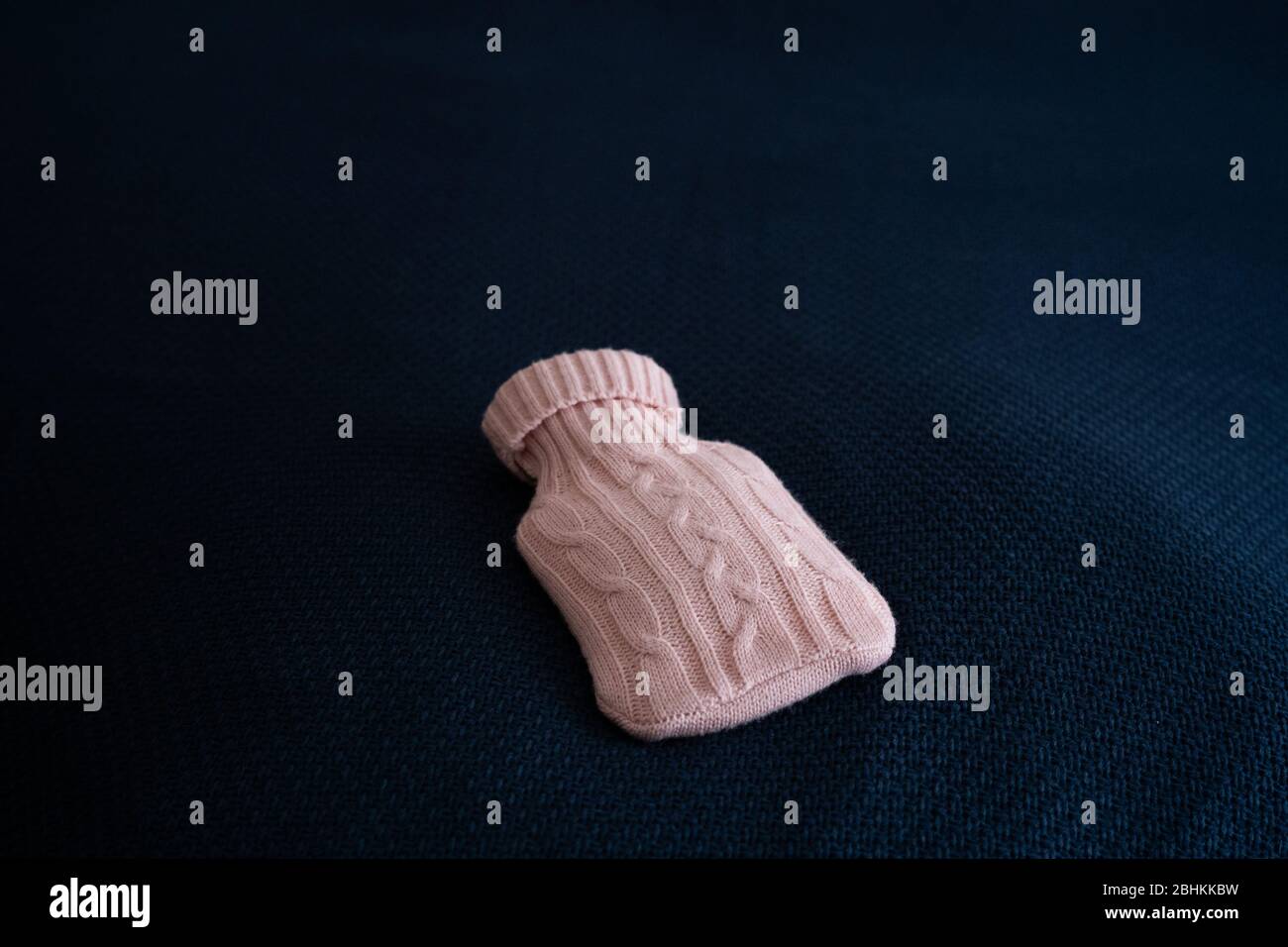 Medizinische Wärmflasche. Medizinische Heizkissen in einem Wollkoffer aus rosa Wolle ruht auf einem Plaid aus blau Stockfoto
