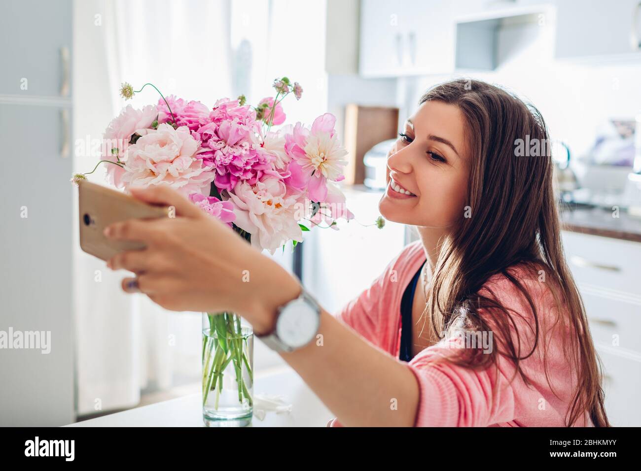 Frau, die Selfie mit Blumenstrauß von Pfingstrosen zu Hause mit dem Smartphone nimmt. Geschenk von Ehemann Stockfoto