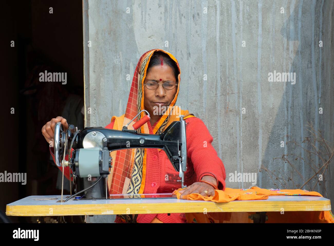 Frau auf einer Nähmaschine, die Kleidung in einem ländlichen indischen Dorf macht Stockfoto