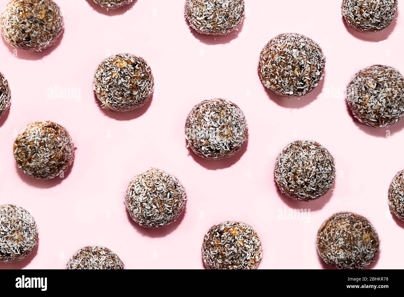 Muster aus Energiebällen mit Hafer, Schokolade und Kokosnuss auf pastellrosa Hintergrund. Gesunde vegane und rohe Ernährung. Richtige Ernährung Konzept. Selektiver Fokus. Kopierbereich. Stockfoto
