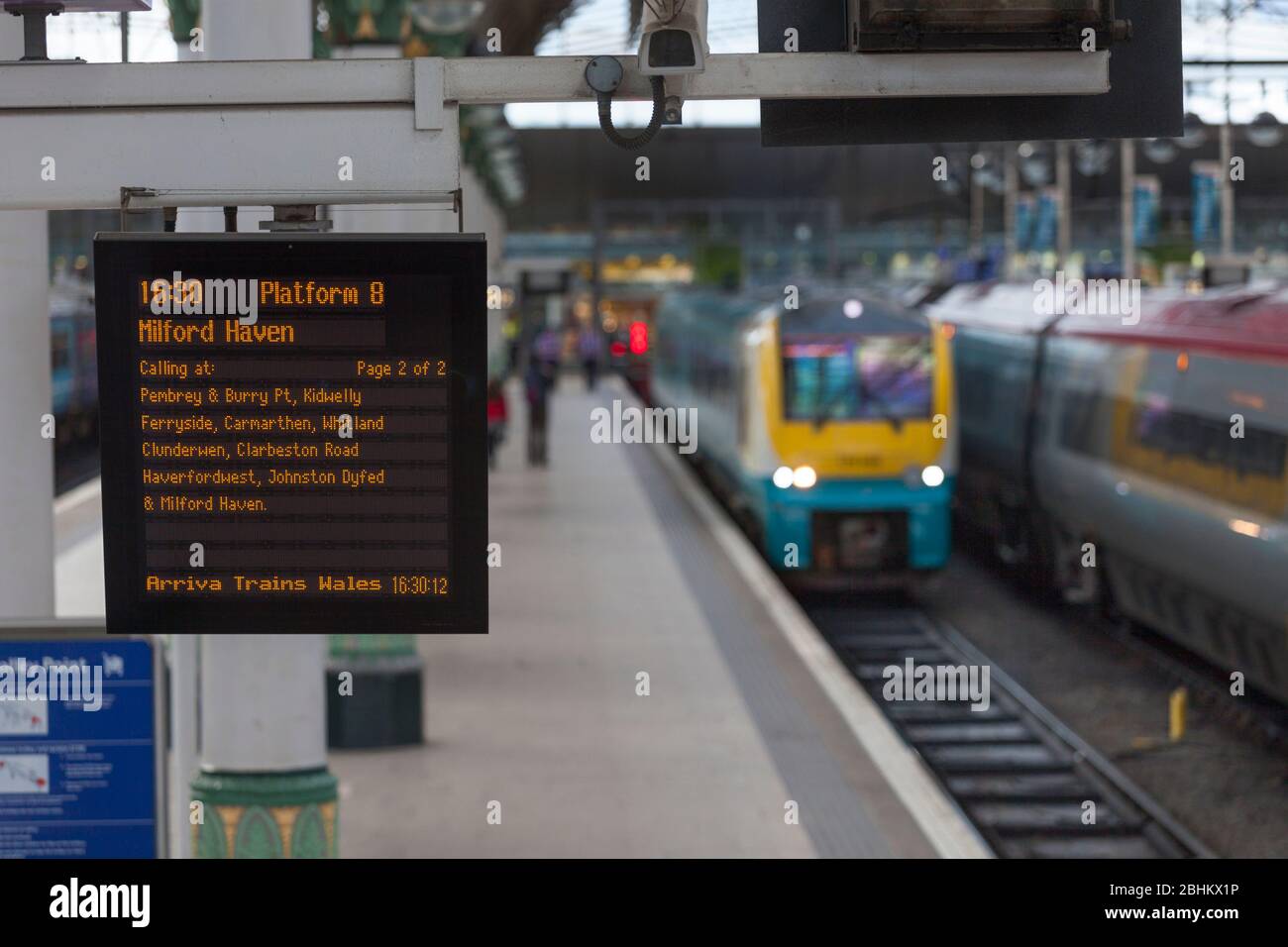 Infopoard für die Zugabfahrt am Bahnhof Manchester Piccadilly mit einem Zug im Hintergrund Stockfoto