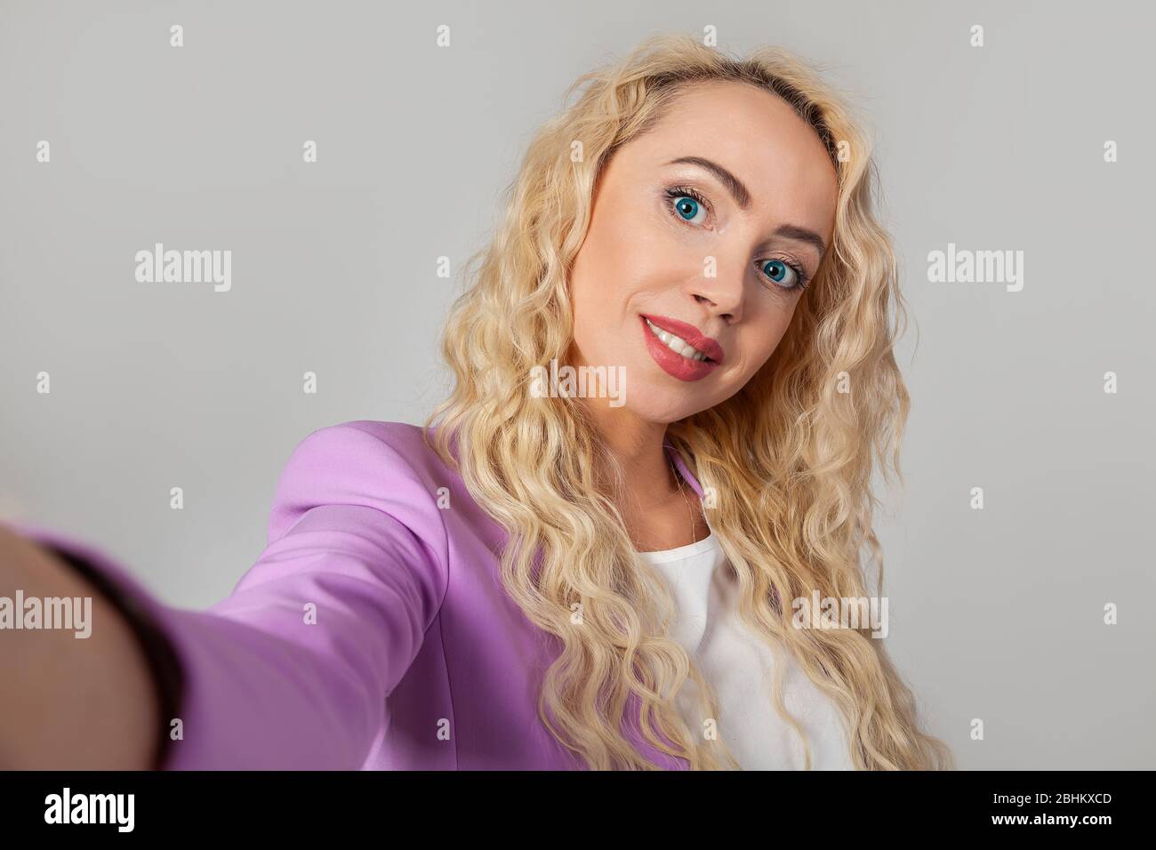 Nahaufnahme Porträt einer stilvollen schönen blonden Frau mit blauen Augen, ein Selfie auf einem Smartphone, Video ruft Freunde durch eine Anwendung, mit einem Lächeln zufrieden, weißen Hintergrund Stockfoto