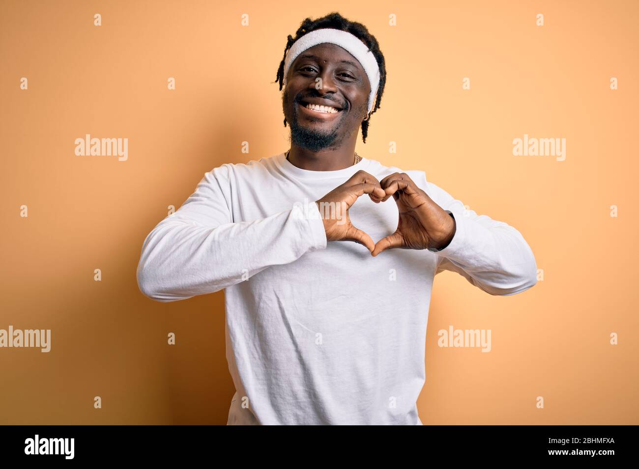 Junger afroamerikanischer Mann, der Sport tut, der Sportswer über isoliertem gelbem Hintergrund trägt, der in der Liebe lächelt, das Herz-Symbol und Form mit den Händen zeigt. Ro Stockfoto